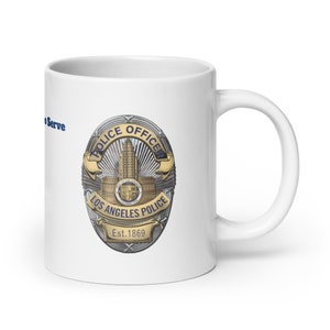 May include: White ceramic mug featuring a blue and gold Los Angeles Police Department badge design. The badge displays the words "Police Officer" and "Los Angeles Police" with the year "Est. 1869" underneath. The badge is encircled by a silver ring with a starburst pattern.