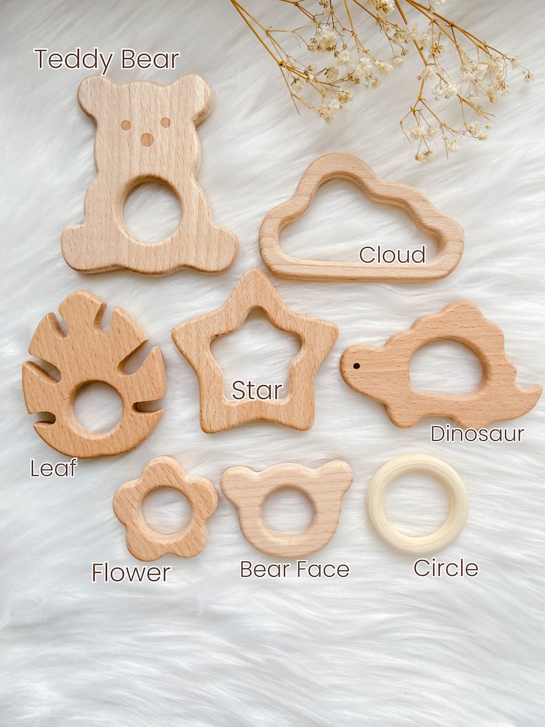 K&ouml;nnte beinhalten: Satz von zehn Holz-Bei&szlig;ringen in verschiedenen Formen, darunter ein Teddyb&auml;r, eine Wolke, ein Stern, ein Blatt, eine Blume, ein B&auml;renkopf, ein Dinosaurier und ein Kreis. Die Bei&szlig;ringe sind aus Naturholz gefertigt und perfekt f&uuml;r Babys zum Kauen.