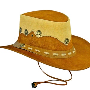 Peut inclure: Un chapeau de cowboy en daim marron avec une bande en daim beige et des accents métalliques décoratifs. Le chapeau a une large bordure et une mentonnière.