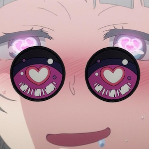 Puede incluir: Primer plano de la cara de un personaje de dibujos animados con mejillas rosadas y ojos grandes. Los ojos están cubiertos con parches circulares negros, rosas y blancos con una forma de corazón en el centro.
