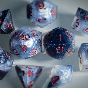May include: A set of ten-sided dice with a galaxy-like pattern and red numbers. The dice are made of a translucent material and have a sparkly finish.