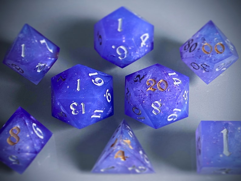 May include: A set of eight purple and blue dice with white and gold numbers. The dice are made of a translucent material and have a speckled appearance. The numbers on the dice are 1, 2, 3, 4, 5, 6, 8, 9, 13, 14, 16, 20, and 61.