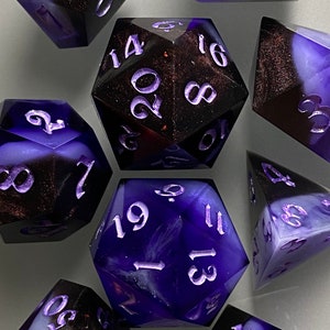 May include: A set of seven purple and black dice with white numbers. The dice are made of a translucent material with a swirling pattern.