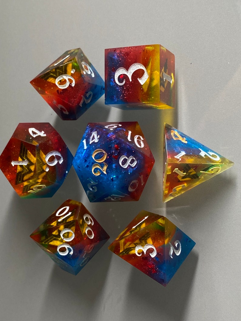 May include: Set of seven polyhedral dice with a rainbow glitter finish. The dice are numbered 1-6, 1-20, 4-sided, 6-sided, 8-sided, 10-sided, and 12-sided. The dice are a mix of red, yellow, blue, and green.