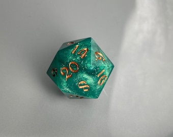 May include: A teal green, glittery, 20-sided dice with gold numbers. The dice is showing the number 14.