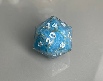 May include: A blue twenty-sided die with gold flecks and white numbers. The die is showing the number 20.