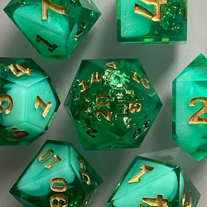 May include: Set of green and white dice with gold numbers and flecks. The dice are in various shapes, including a d20, d12, d10, d8, d6, and d4.