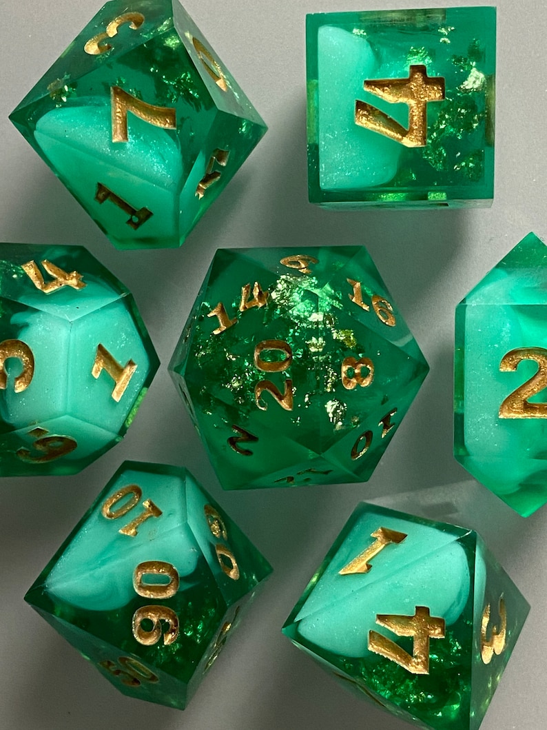 May include: Set of green and white dice with gold numbers and flecks. The dice are in various shapes, including a d20, d12, d10, d8, d6, and d4.