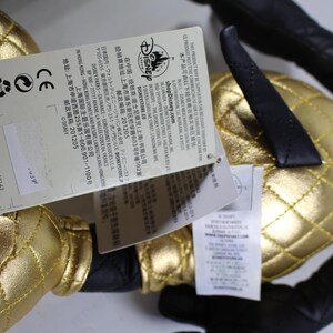 May include: A black and gold plush toy with a quilted design. The toy has a tag attached with the Disney logo and text in Japanese and English. The text on the tag includes the website shopDisney.com and the address of the Disney Store in Shanghai, China.