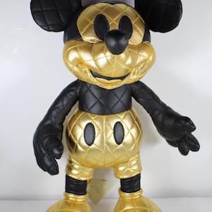 May include: A black and gold quilted Mickey Mouse plush toy. The toy is wearing a gold quilted outfit with black accents. The toy has a black nose and black eyes.
