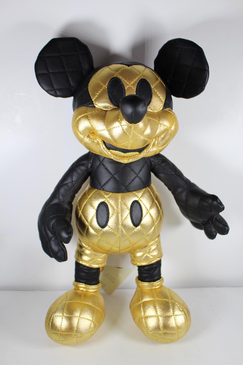 May include: A black and gold quilted Mickey Mouse plush toy. The toy is wearing a gold quilted outfit with black accents. The toy has a black nose and black eyes.