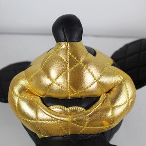 May include: A black and gold plush toy shaped like Mickey Mouse. The toy has a quilted design and a shiny gold finish.