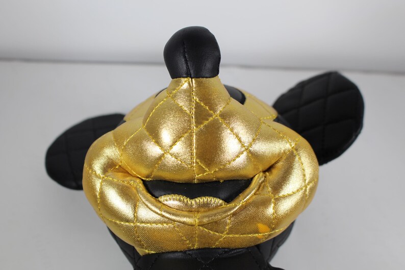 May include: A black and gold plush toy shaped like Mickey Mouse. The toy has a quilted design and a shiny gold finish.
