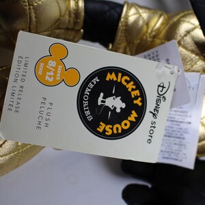 May include: Gold Mickey Mouse plush toy with a black quilted fabric. The tag reads "Disney Store Mickey Mouse Memories Plush Limited Release Edition Limit&eacute;e 8/12 Series".