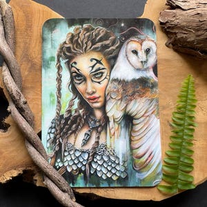 Può includere: Una stampa artistica rettangolare raffigurante una donna con intricati segni sul viso e capelli intrecciati, accanto a un gufo bianco. La donna indossa un top argentato dettagliato. L'opera d'arte ha un tema mistico, con uno sfondo verde chiaro e blu.