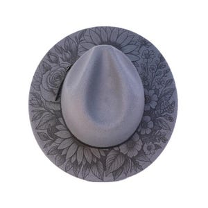 May include: A grey fedora hat with a floral design. The hat has a grey crown and brim, with a black leather band. The brim is decorated with an intricate pattern of flowers and leaves, creating a stylish accessory.