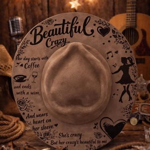 May include: A tan felt fedora hat featuring black laser-engraved text and illustrations. The text reads: Beautiful Crazy, Her day starts with coffee and ends with a wine, And wears heart on her sleeve, She's crazy, But her crazy's beautiful to me.
