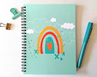 A5 spiral bound notebook, with grid paper pages and decorated with a whimsical rainbow and clouds design