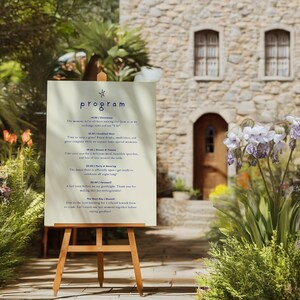 Peut inclure: Une pancarte blanche avec une étoile bleue et le mot "programme" en lettres bleues. La pancarte liste un programme d'événements pour un mariage, incluant une cérémonie, un cocktail, un dîner, des danses et un brunch d'adieu. La pancarte est sur un chevalet devant un bâtiment en pierre avec une porte en bois.