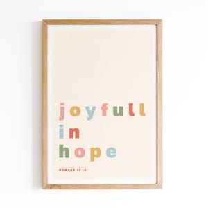 May include: A framed print with a beige background and the text "joyful in hope" in colorful letters. The text "ROMANS 12:12" is printed in smaller letters below the main text.