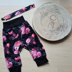 Könnte beinhalten: Schwarze und rosa Baby-Leggings mit Erdbeer- und Macaron-Druck. Die Leggings haben einen schwarzen Bund und einen Clip-Schnullerhalter.