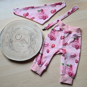 Könnte beinhalten: Rosa Baby-Leggings mit einem Muster aus Macarons und Erdbeeren. Die Leggings haben einen rosa-weißen Saum.