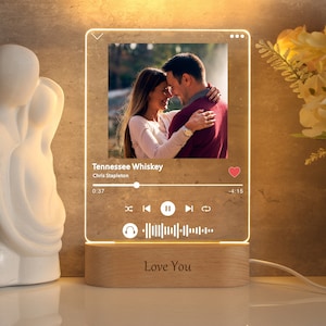 May include: A clear acrylic light-up sign with a photo of a couple embracing. The sign has a music player interface with the song "Tennessee Whiskey" by Chris Stapleton playing. The sign also has the text "Love You" on the base.