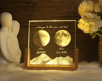Op de afbeelding: Een verlichte glazen plaquette met een houten frame, met twee manen en de tekst "i love you to the moon and back". De manen zijn gelabeld "Chuck" en "Miss" met de data "July 25 1996" en "September 26 1996".
