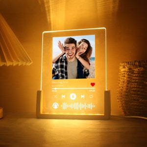 Könnte beinhalten: Personalisiertes LED-Nachtlicht mit einem Foto eines Paares. Das Licht hat einen Holzsockel und eine transparente Acrylplatte mit einem gedruckten Bild und einer Musikplayer-Oberfläche. Der Songtitel lautet "Bleeding Love" von Leona Lewis.
