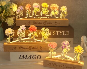 May include: A set of two wooden light-up flower displays with the text "Grandma's Garden" and "Mom's Garden" engraved on the base. Each display features a row of colorful flowers with names like "Chloe", "Grace", and "Emily" printed on the flowers.