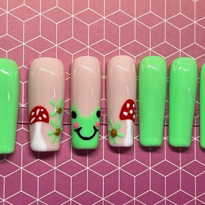 Può includere: Set di otto unghie acriliche lunghe, verdi e rosa con un design di rana, fungo e fiore.