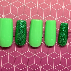 Può includere: Cinque unghie finte verdi, due sono verdi solide e tre hanno glitter verde.