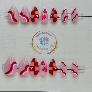 May include: Oval-shaped press-on nails in various designs. Some nails feature a pink base with red and white wavy lines, while others have a red and white checkerboard pattern or pink hearts. The logo "MomsNails.com" is visible.