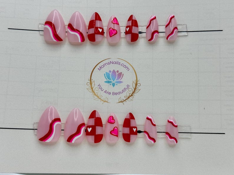 May include: Oval-shaped press-on nails in various designs. Some nails feature a pink base with red and white wavy lines, while others have a red and white checkerboard pattern or pink hearts. The logo "MomsNails.com" is visible.