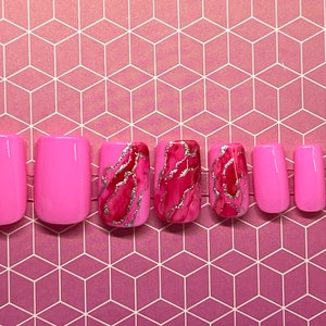 Può includere: Set di unghie finte quadrate di colore rosa e rosso con un designo marmoreo. Alcune unghie sono di colore rosa solido, mentre altre hanno un designo marmoreo rosa e rosso con accenti di glitter argentati.