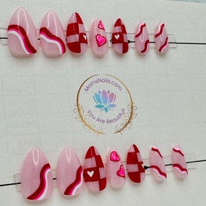May include: A set of almond-shaped press-on nails in various designs. Some nails feature a pink base with red and white wavy stripes, while others have a red and white checkered pattern or pink hearts.