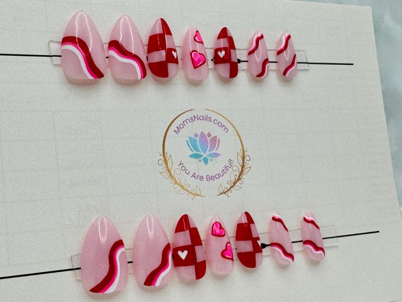 May include: A set of almond-shaped press-on nails in various designs. Some nails feature a pink base with red and white wavy stripes, while others have a red and white checkered pattern or pink hearts.
