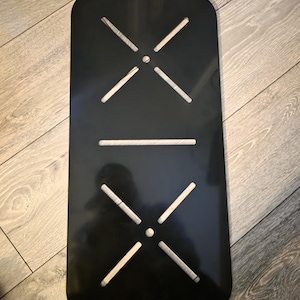 May include: A black rectangular object with rounded corners, featuring white cross-shaped cutouts and a horizontal line cutout. It is positioned on a wooden surface.