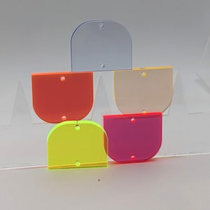 Könnte beinhalten: Eine Sammlung von fünf farbigen, halbkreisförmigen Acryl-Anhängern. Die Anhänger sind in den Farbtönen Orange, Gelb, Pink, Hellblau und Creme gehalten. Jeder Anhänger hat zwei kleine Löcher zum Befestigen. Die Anhänger sind in einer gestapelten Formation angeordnet.