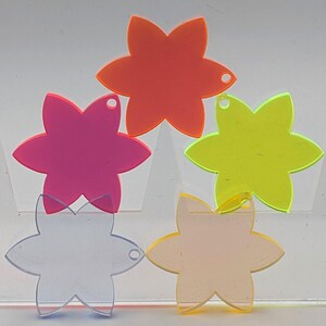 Könnte beinhalten: Fünf blütenförmige Acrylzuschnitte in verschiedenen Farben: Orange, Pink, Gelb, Klar und Pfirsich. Jede Blume hat sechs Blütenblätter und ein kleines Loch zum Aufhängen. Geeignet für Bastelarbeiten oder Dekorationszwecke.