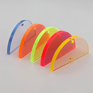 Könnte beinhalten: Eine Reihe von fünf halbkreisförmigen, transparenten Acrylteilen in verschiedenen Farben: Blau, Orange, Grün, Rot und Gelb. Jedes Teil hat ein kleines Loch oben. Die Teile sind in einer Reihe angeordnet, um ihre leuchtenden Farben zu zeigen.