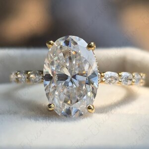 May include: A gold engagement ring featuring an oval-shaped diamond centre stone and a band of smaller diamonds.
