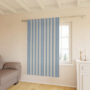 May include: A blue and white striped curtain hangs in front of a window. The curtain has vertical stripes of light blue and off-white. The curtain is hanging on a silver rod. The room has a neutral color palette.