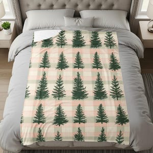 May include: A rectangular throw blanket featuring a repeating pattern of dark green pine trees arranged in rows. The background consists of a soft plaid design with intersecting horizontal and vertical lines in shades of pale pink and cream.