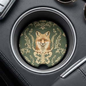 May include: A circular car cup holder coaster featuring a detailed illustration of a fox head centered against a dark green background with a light beige ornate damask pattern. The coaster has a small notch along the bottom edge for easy removal.