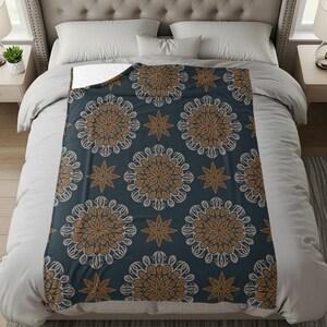 Peut inclure: Un plaid rectangulaire présentant un fond bleu marine foncé avec un motif répétitif de grands designs circulaires complexes en forme de mandala dans des tons marron et gris clair, entremêlés de petites étoiles à huit branches.