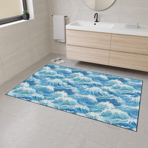 Könnte beinhalten: Eine rechteckige Badematte mit einem sich wiederholenden Muster stilisierter Meereswellen in Blau- und Weißtönen. Die Matte hat einen schwarzen Rand und liegt auf einem gefliesten Boden in einem Badezimmer. Das Design erinnert an das Meer.