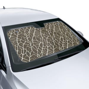 May include: A car windshield sun shade featuring a brown background with a white, branching, vein-like pattern that resembles a leaf skeleton or cracked earth. The shade is positioned inside the front windshield of a white vehicle.