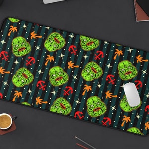 Op de afbeelding: Een zwarte en groene bureau mat met een herhalend patroon van een schepsel uit de zwarte lagune, palmbomen, ankers en sterren.