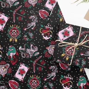 May include: Black and white wrapping paper with a repeating pattern of traditional tattoo designs. The designs include roses, hearts, anchors, tigers, snakes, and frogs. The background is black with white polka dots.